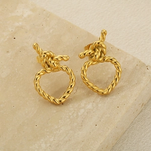 Détails macro des boucles d'oreilles nœud torsadé doré sur fond de pierre naturelle