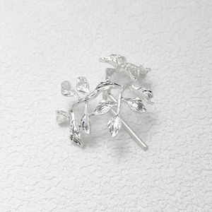 Close-up of silver metal leaf hair hook with fine texture on white textured background