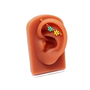 Détail du piercing industriel doré avec pendentifs fleurs bleues et jaunes sur modèle d'oreille