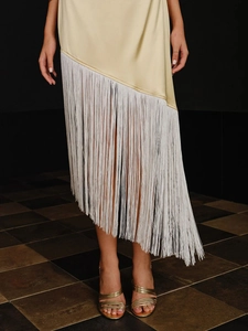 Detail of champagne satin dress featuring white fringe tassels and asymmetrical hemline