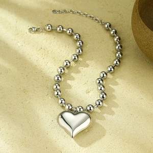 Polished silver heart pendant necklace with beaded chain on stone surface