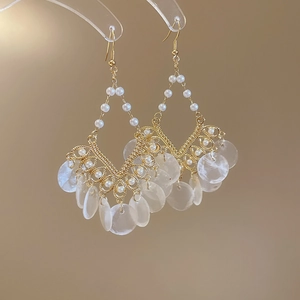 Close-up of golden shell fringe earrings with white pearls on a display stand