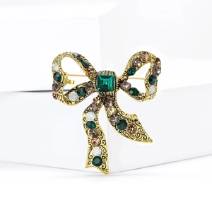 Vintage bronze bow brooch with green crystal and rhinestones on white background