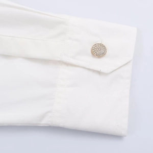 Detailed macro view of a white poplin shirt cuff featuring a luxury gold diamond button