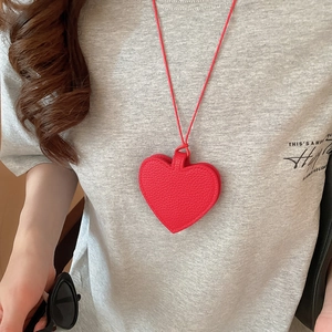 Macro shot of red heart pendant with lychee grain leather texture on grey sweater