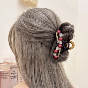 Detail showing an elegant red bead and white flower hair claw on a half-up hairstyle