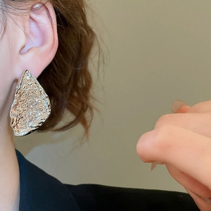 Detail of silver drop earrings with a hammered texture and irregular metallic finish