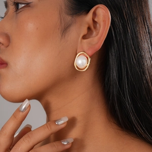 Detail of gold-plated pearl stud earring with minimalist floral frame on a model ear