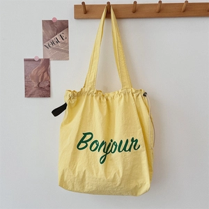 Detail of a bright yellow drawstring tote bag with green Bonjour print on a wall hook