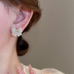Detail of bow earrings with faux pearls and rhinestones on model's ear in golden finish