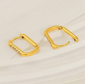 Macro shot of U-shaped gold earrings with sparkling pavé stones on cream wavy tray