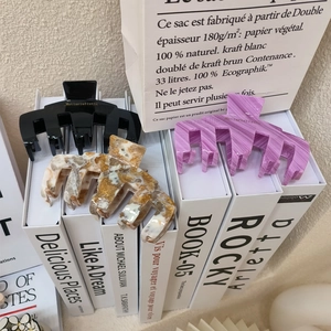 Vue détaillée de pinces à cheveux en acétate noires, marbrées et violettes sur livres
