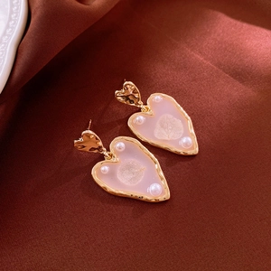 Detailed macro view of heart-shaped gold earrings with pink resin and pearl accents