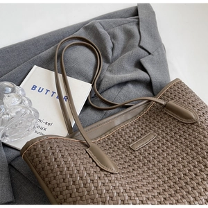 Detail view of a brown woven tote bag placed on a grey blazer with stylish accessories