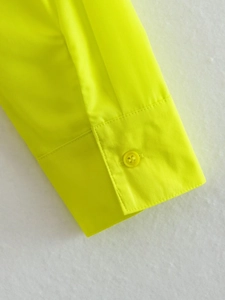 Gros plan du poignet d'une chemise jaune fluo avec bouton en résine et tissu tissé