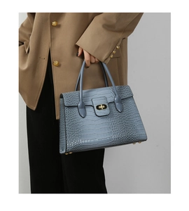 Detail of light blue crocodile texture handbag with gold clasp on female model