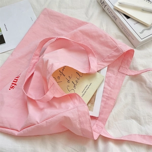 Bolso tote de lona rosa sobre sábanas blancas con libros y textura detallada