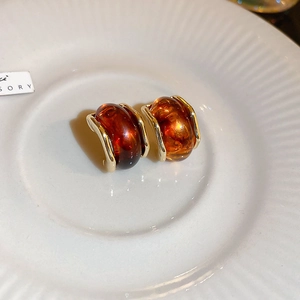 Macro shot of amber resin C-shaped earrings with gold metal edges on a white tray