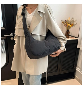 Détail du sac croissant matelassé noir porté par un mannequin en trench-coat beige
