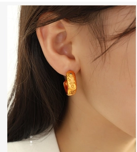 Detailed macro view of gold sunflower and star embossed hoop earrings with a black stone
