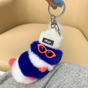 Close-up of a blue and white plush caterpillar keychain with a white knit hat and glasses