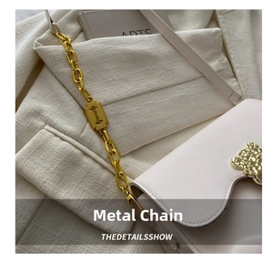 Detail of cream shoulder bag featuring gold chain with razor blade charm and bear clasp