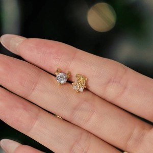 Macro shot of asymmetric gold Christmas earrings with reindeer and gift box on finger