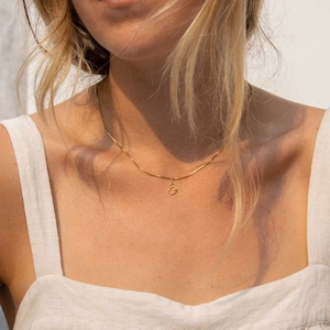 Primo piano della collana dorata con ciondolo lettera E sulla clavicola