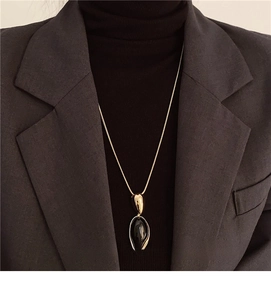 Detailed view of an oval black resin pendant on a long gold chain with a dark knit sweater