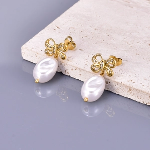 Elegant gold bow earrings with zircon diamonds and pearl drop on stone surface