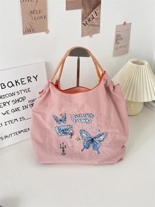 Detail of pink embroidered tote bag featuring blue butterfly and braided handle straps