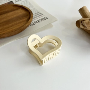 Detail of elegant cream heart-shaped hair claw on a wooden tray with a minimalist aesthetic