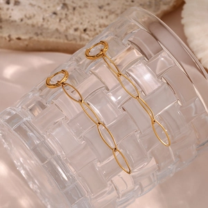 Macro detail of 18K gold plated long chain link earrings on a textured glass rim