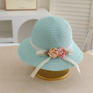 Detail of mint green straw sun hat featuring white lace ribbon and fabric floral accents