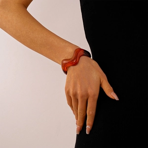 Detailed view of amber acrylic bangle with wavy texture on model's wrist against light background