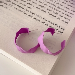 Detail of purple wavy hoop earrings with matte finish resting on an open book