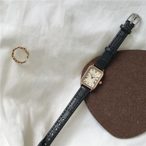 Detail of square rose gold watch with black leather strap on a textured brown surface