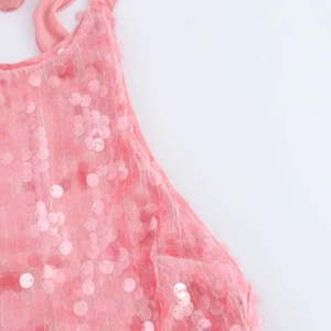 Dettaglio ravvicinato delle paillettes rosa sull'abito corto con schiena scoperta e lacci