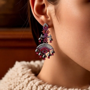 Detailed view of bohemian fan-shaped drop earrings with red gems and tassels on a model
