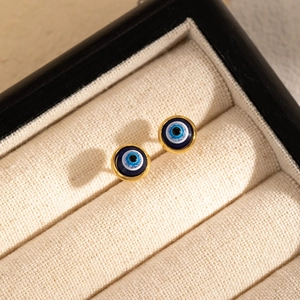 Detailed view of gold-rimmed evil eye stud earrings placed in a luxury jewelry box