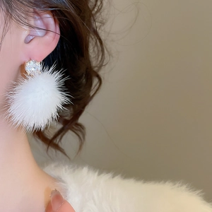 Gros plan de boucles d'oreilles pompons blancs avec clous en zircon portées par un mannequin