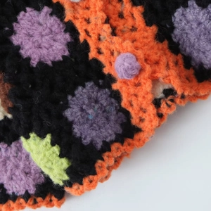 Macro view of handmade crochet sweater showing colorful floral embroidery on black yarn