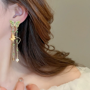 Close-up of elegant butterfly tassel earrings with zircon, green beads and white pearls