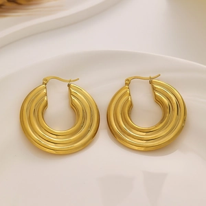Detail of gold-plated titanium C-shaped hoop earrings with three-ribbed texture on white plate
