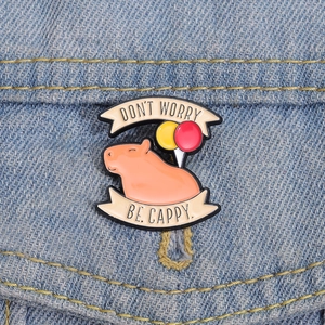 Detail of capybara enamel pin on denim jacket with Don't Worry Be Cappy text