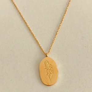 Detail of a gold stainless steel necklace featuring an oval engraved birth month flower pendant