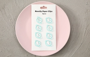 Detail of 8 light blue planet-shaped paper clips on white card in a pink ceramic tray