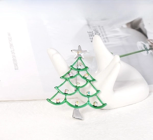 Close-up of a green enamel Christmas tree brooch with colorful rhinestones on a hand prop