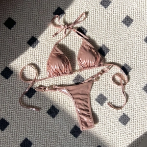 Detail of rose gold bikini set with decorative pearls and metallic rings on side ties