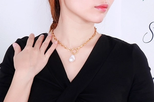 Close-up of gold chain necklace with large white baroque pearl pendant on model